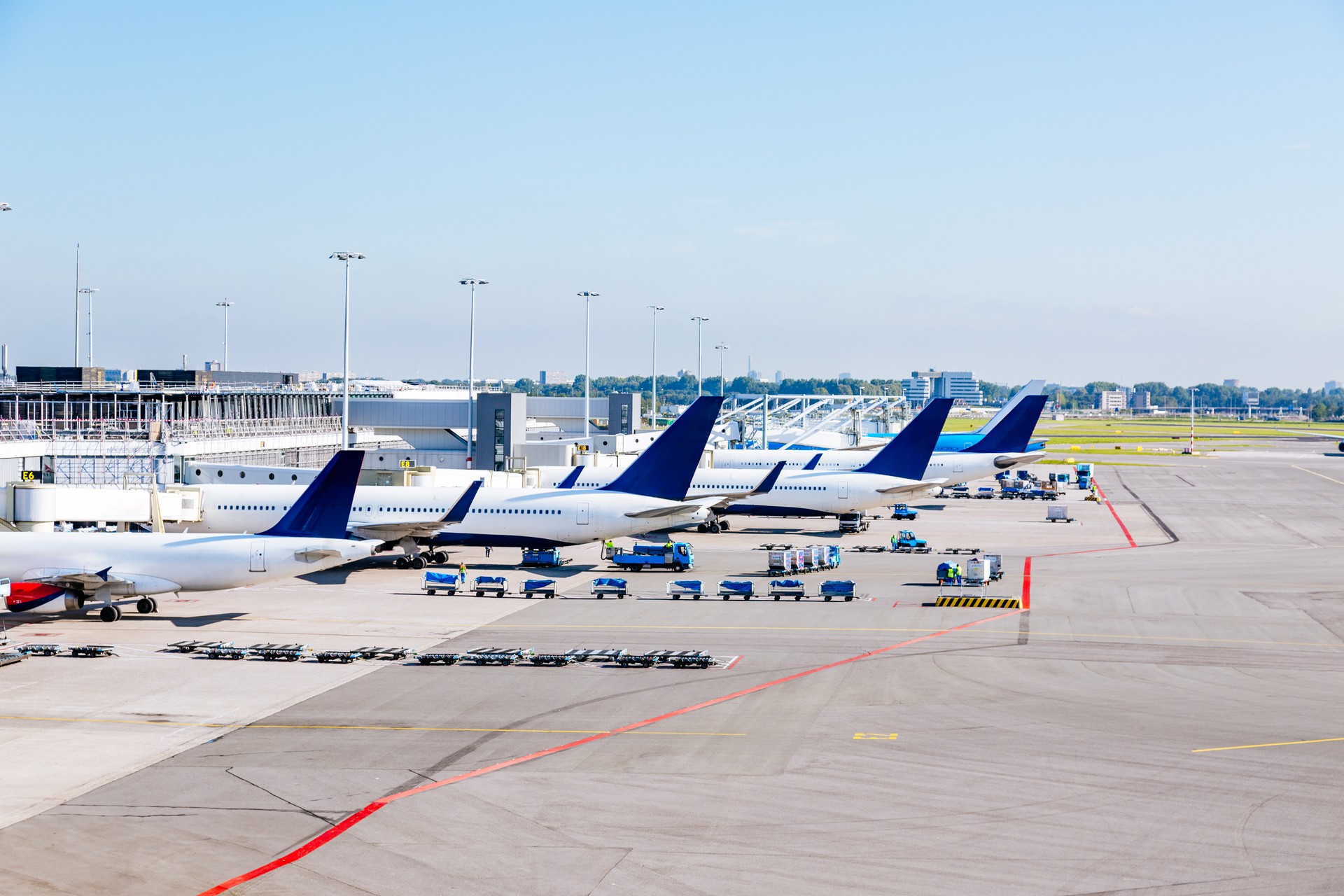 Airplanes parked at the gates of an airport tarmac with a terminal building in the background.